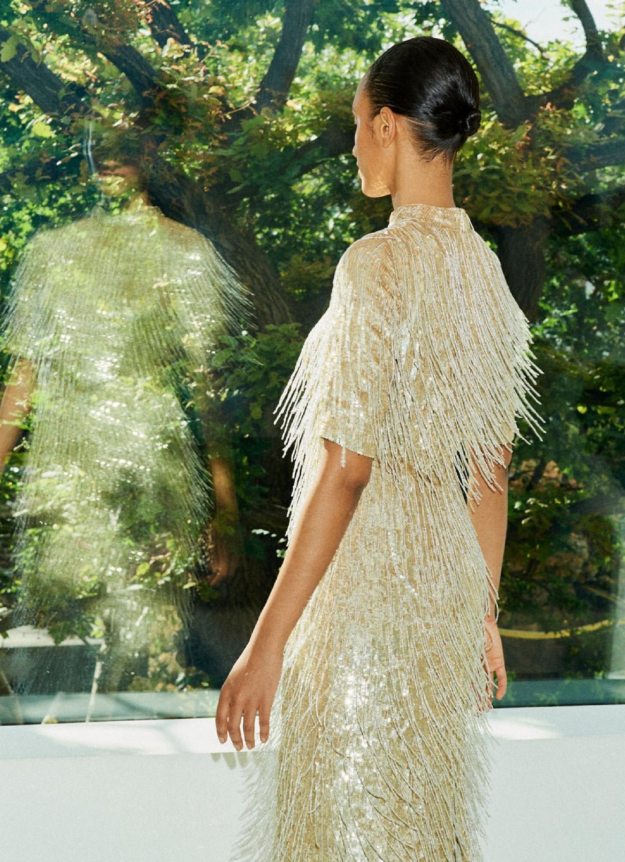 A still image of a woman moving, wearing a hand beaded dress, with the movement showcasing the detail of the beaded elements of the dress regre