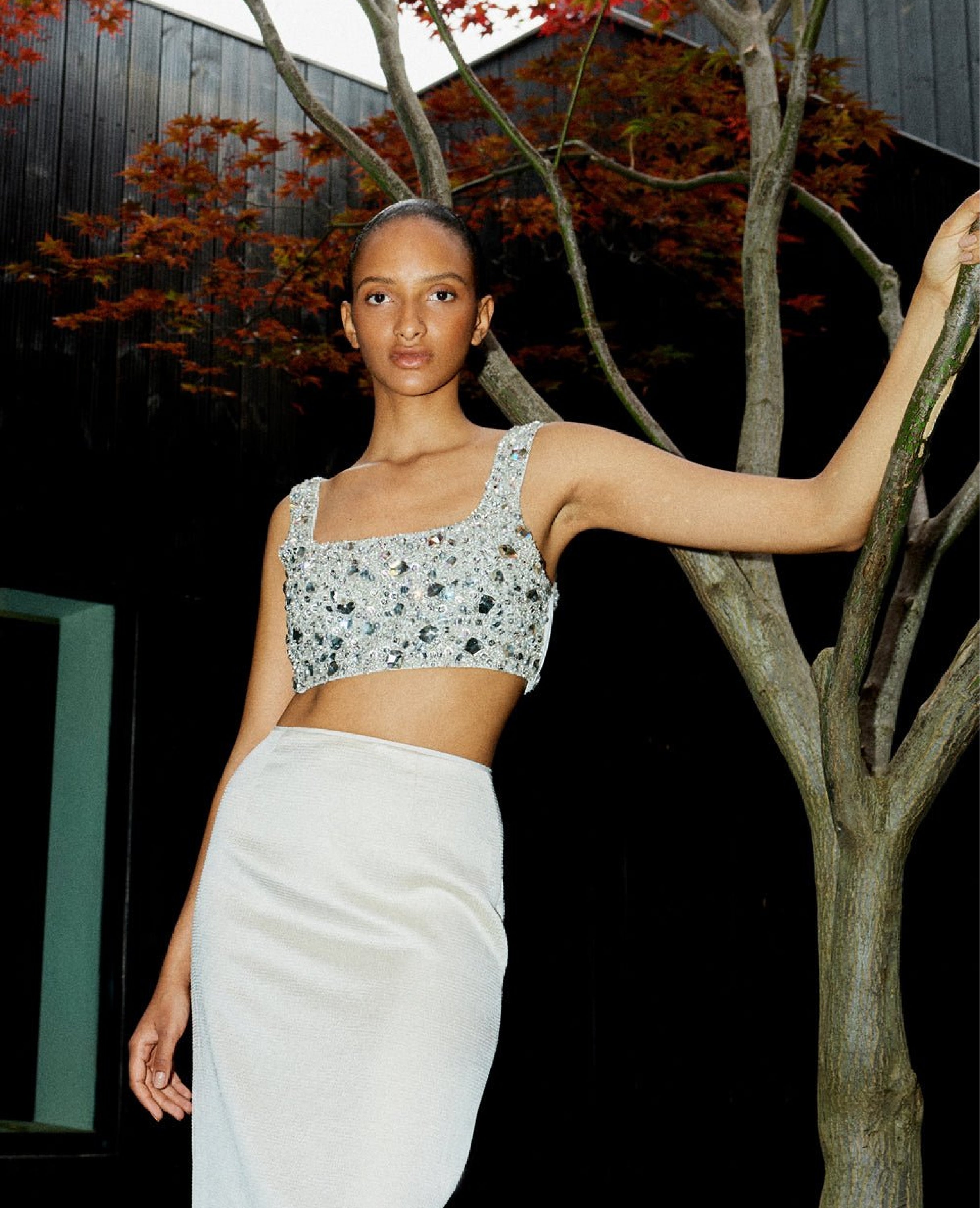 A woman standing next to a tree in a white long skirt and embellished short top by Ilta Studio